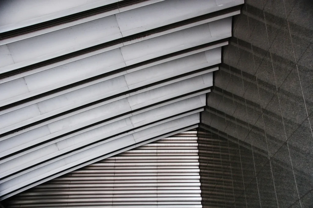 An abstract, close-up view of a modern building showing layered metallic roofing and geometric gray wall panels, illustrating professional commercial roofing installation.