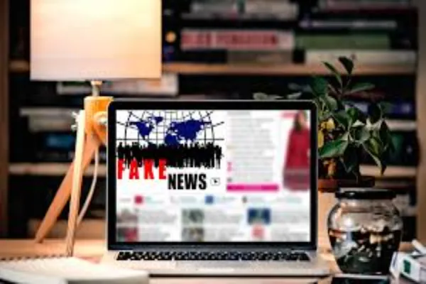 Laptop screen displaying "FAKE NEWS" with blurred content, placed on a desk with a lamp and plant