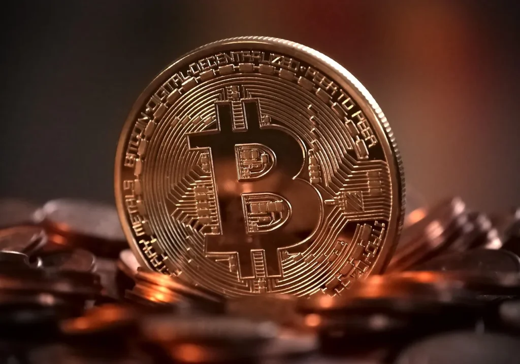 Close-up of a shiny gold Bitcoin coin standing upright amongst a pile of other cryptocurrency coins.