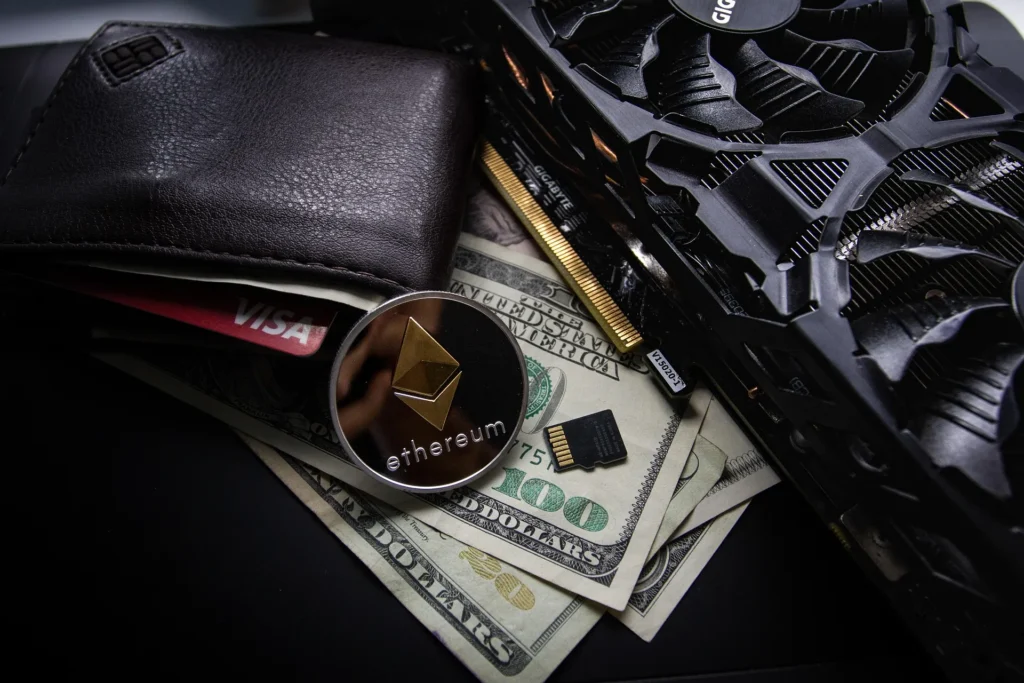 A physical Ethereum coin resting on US dollar bills next to a leather wallet and a powerful computer graphics card, symbolizing cryptocurrency trading and mining.