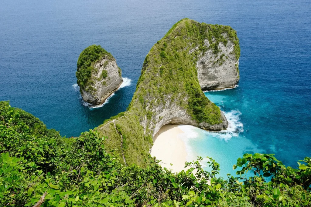 Aerial view of the T-Rex shaped limestone cliffs at Kelingking Beach, Nusa Penida, Bali, featuring white sand and turquoise ocean water.