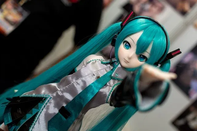 A close-up, angled shot of a high-end Hatsune Miku Dollfie Dream ball-jointed doll wearing her signature teal pigtails and futuristic grey and teal outfit.